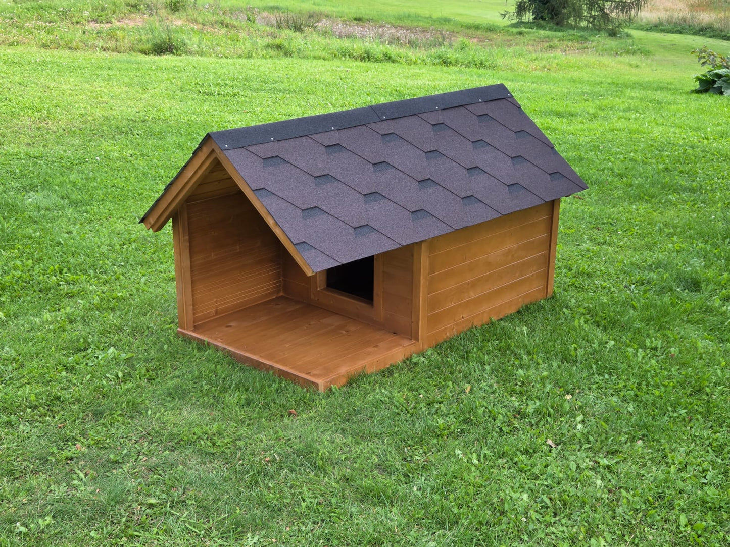 Wooden dog house with a black roof on a grassy field