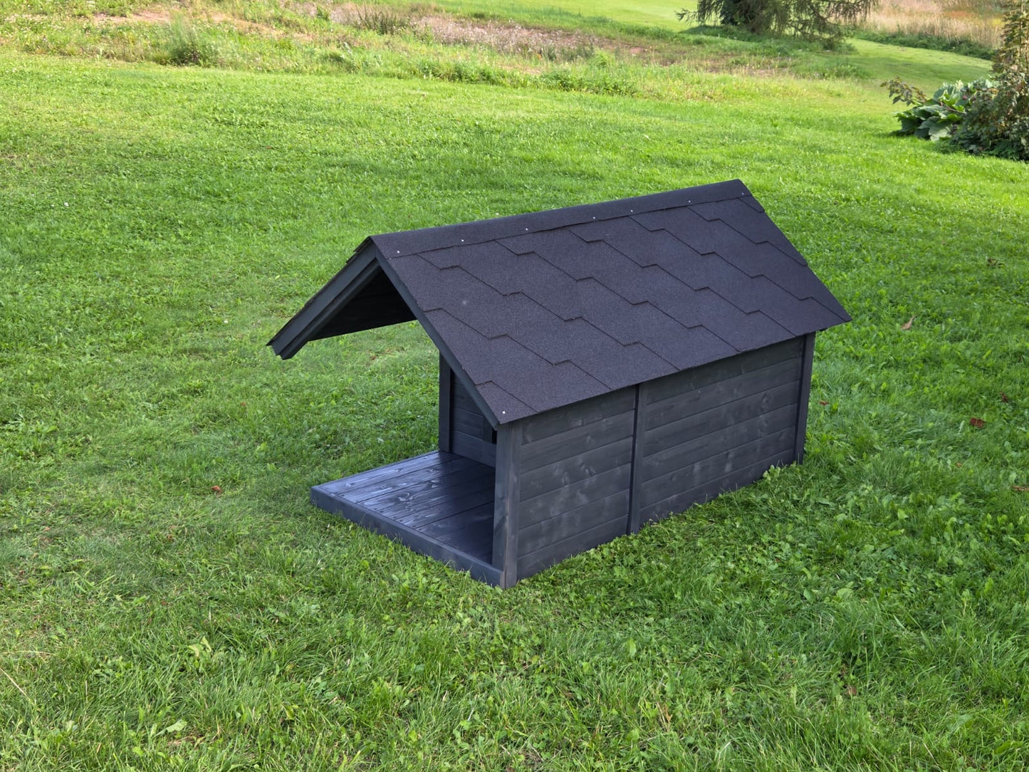 Black dog house on a grassy field