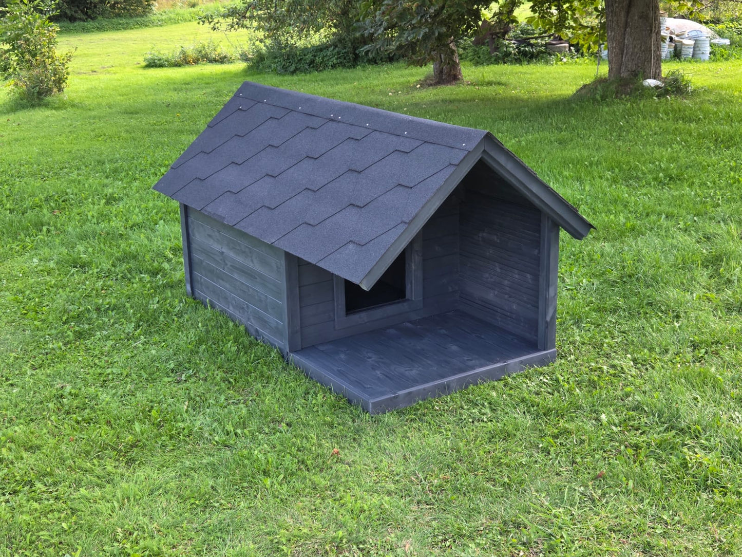 Dark gray dog house on a grassy area with trees in the background