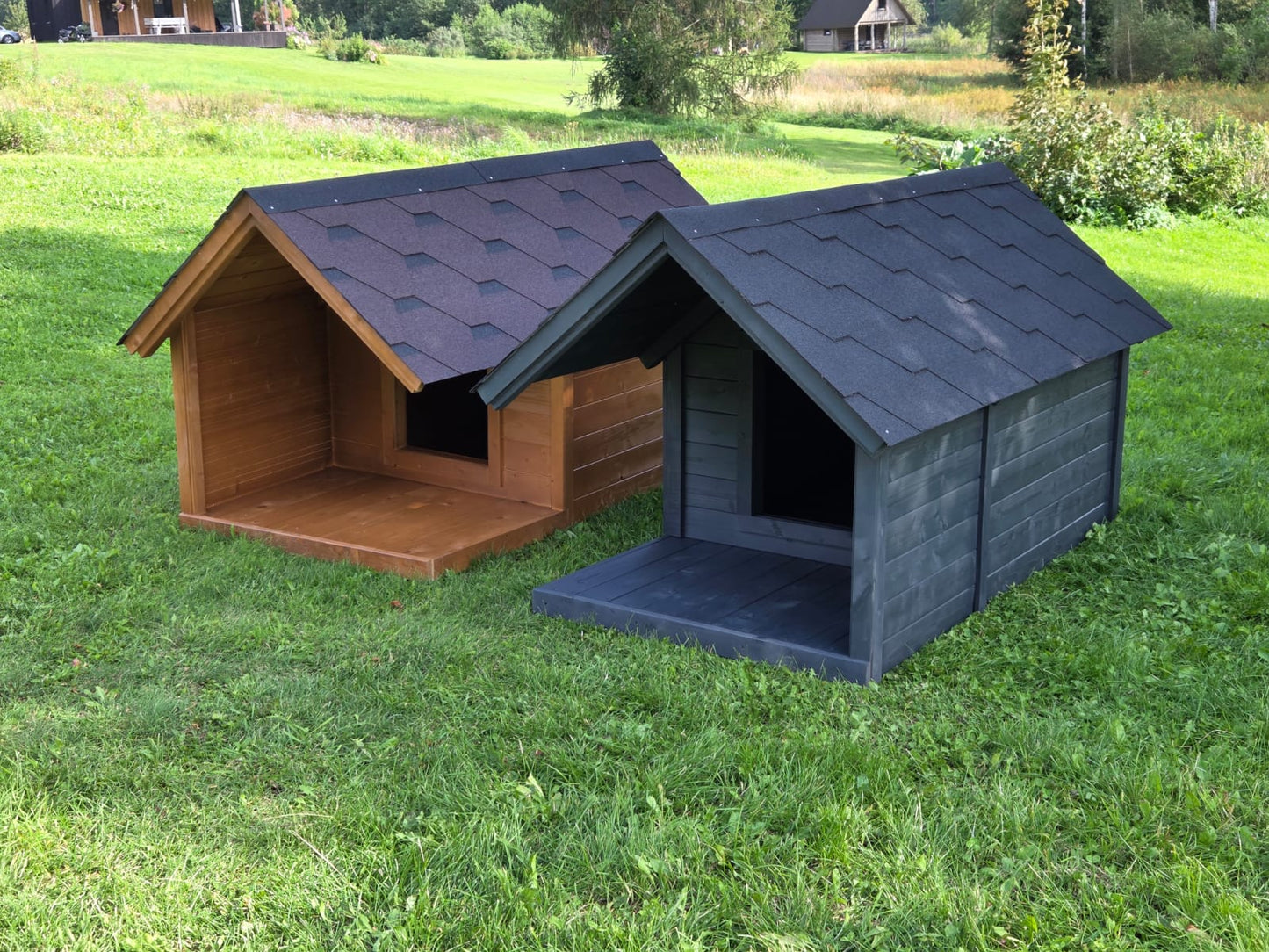 Two wooden dog houses, one brown and one gray, on a grassy field.