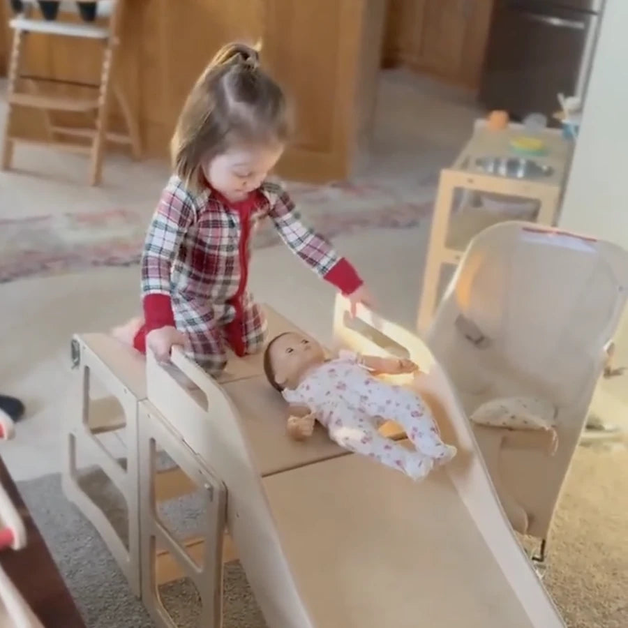 A toddler sending her doll down the birch slide