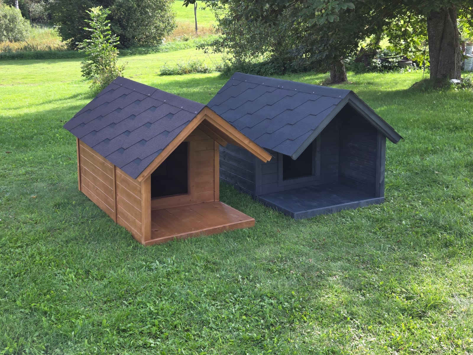 Two dog houses, one brown and one blue, on a grassy area with trees in the background.