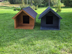 Two dog houses, one brown and one black, on a grassy field with trees in the background.