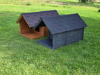 Two dog houses, one brown and one gray, on a grassy field.