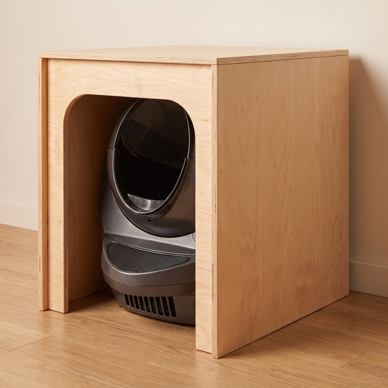 The automatic litter robot hidden inside the birch cover, seen through the arched side entrance - the cover turns the machine into furniture.